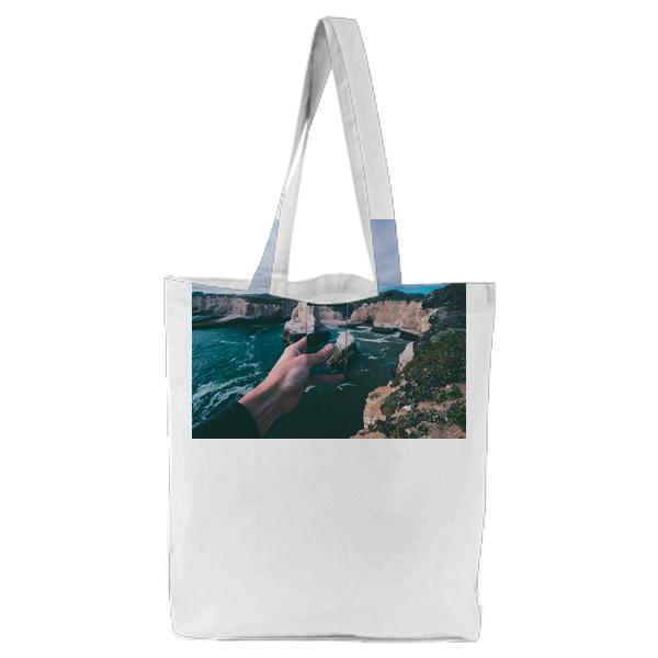 Person Holding Smartphone Capturing Pictures Of Body Water Beside Rock Formations Under Cloudy Sky During Daytime Tote Bag