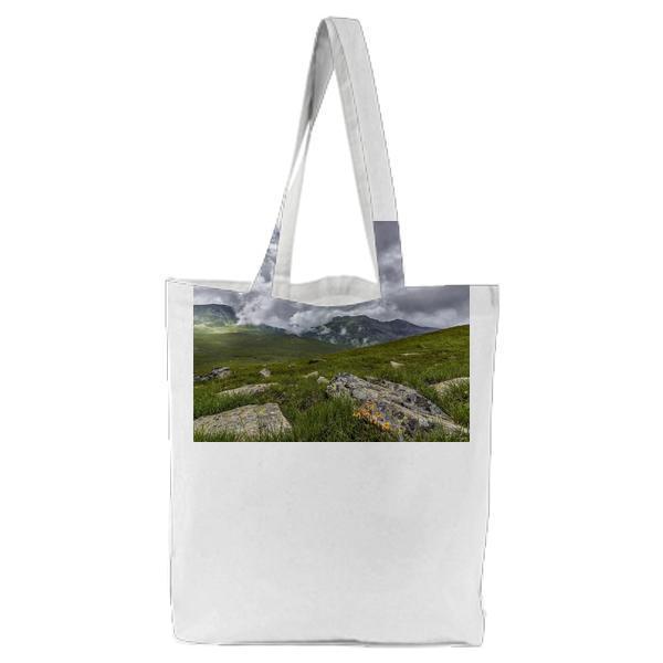 Green Grass Field With Rocks Near Mountains During Cloudy Daytime Sky Tote Bag