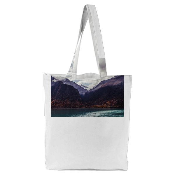 Teal Sea In Front Of Brown Mountains Under Blue Sky Covered White Clouds During Daytime Tote Bag
