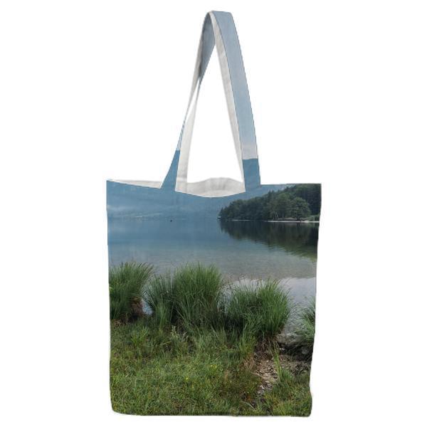 Green Grass Near Body Of Water Under Blue Sky During Daytime Tote Bag