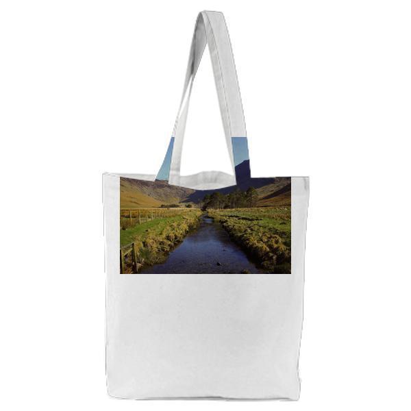 River In Between Grass Field Overlooking Mountain Under Clear Sky During Daytime Tote Bag