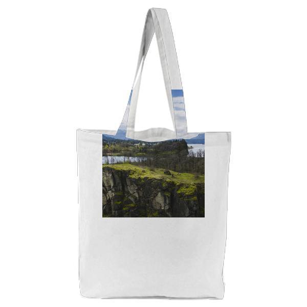 Green Ground Cliff Near Water Under Blue White Sky Tote Bag