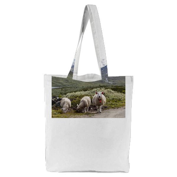 3 White Sheep Standing Near On Green Grass In Front Of Mountains Tote Bag